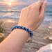 Blue seed bead Kumihimo bracelet on wrist by the ocean, handmade glass bead bracelet inspired by coastal colors